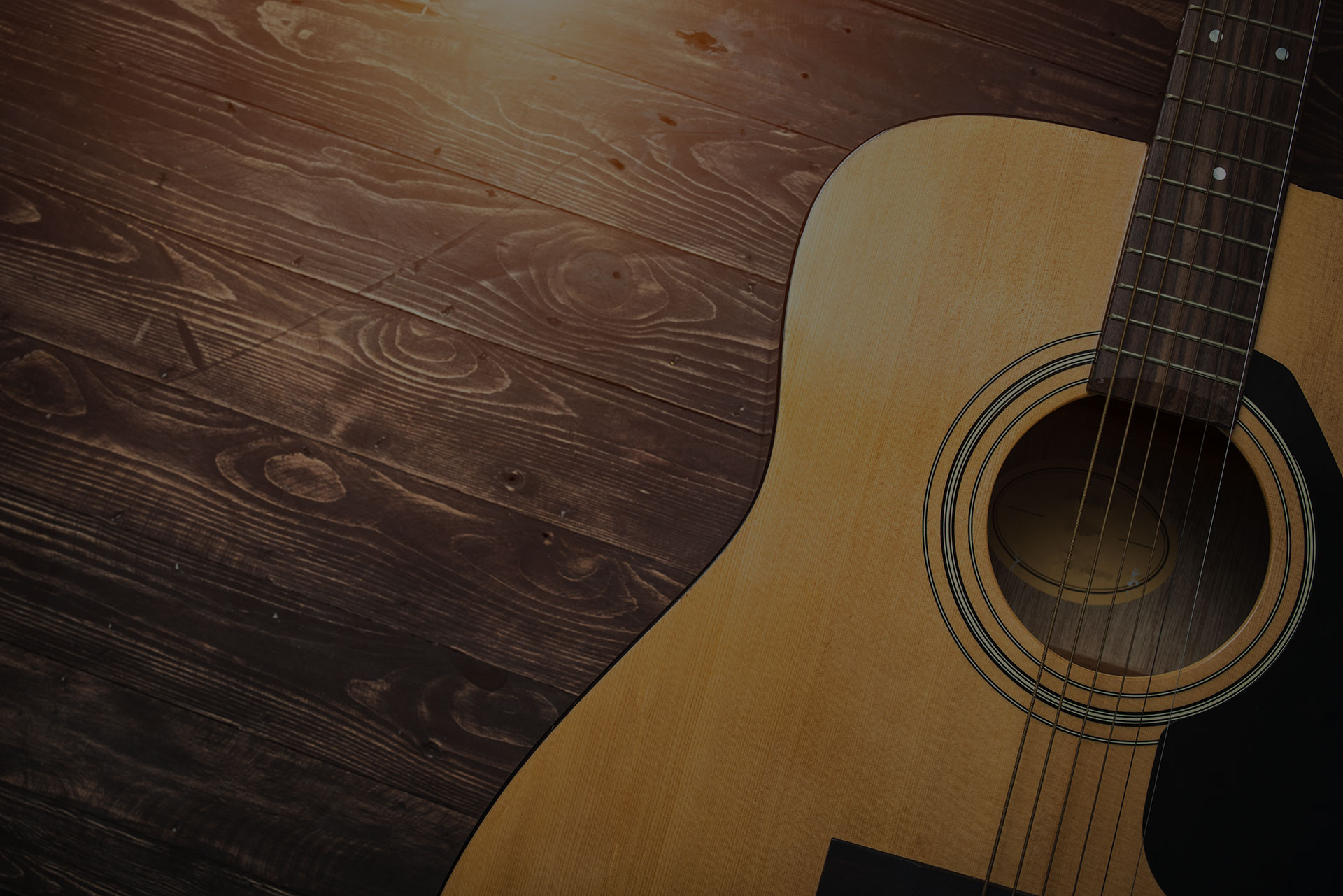 Acoustic guitar resting against a wooden background with copy space